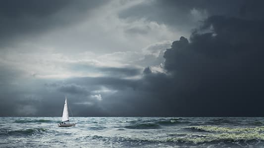 A wide angle of a sailboat navigating through harsh conditions.